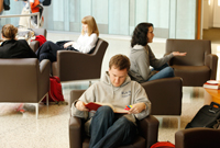 Students sit in armchairs in a study area, some with books, some with computers, some having conversations