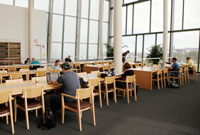 Students sit at study tables in a study area with many windows